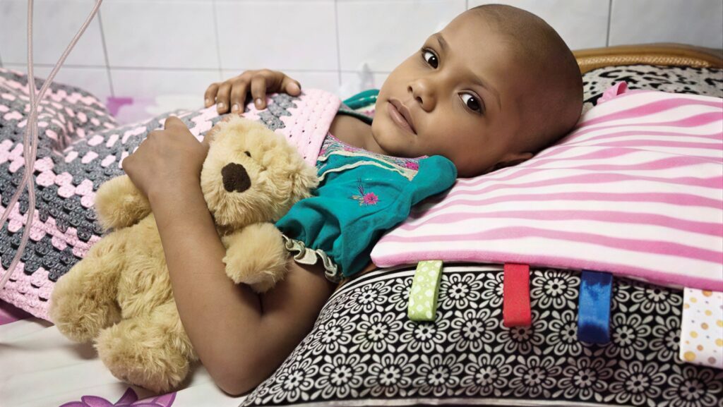 A young child resting in a hospital bed with a teddy bear